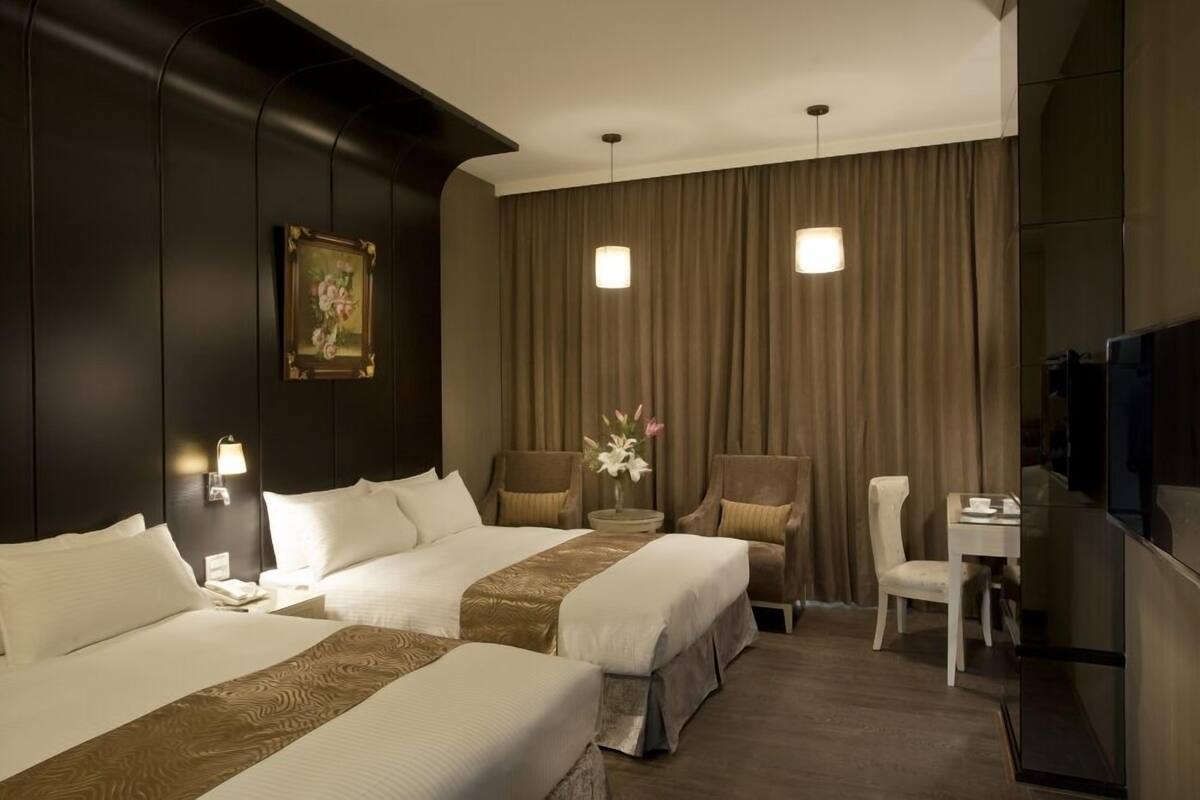 A hotel room with two beds, a desk, a chair, a television, and a painting on the wall.