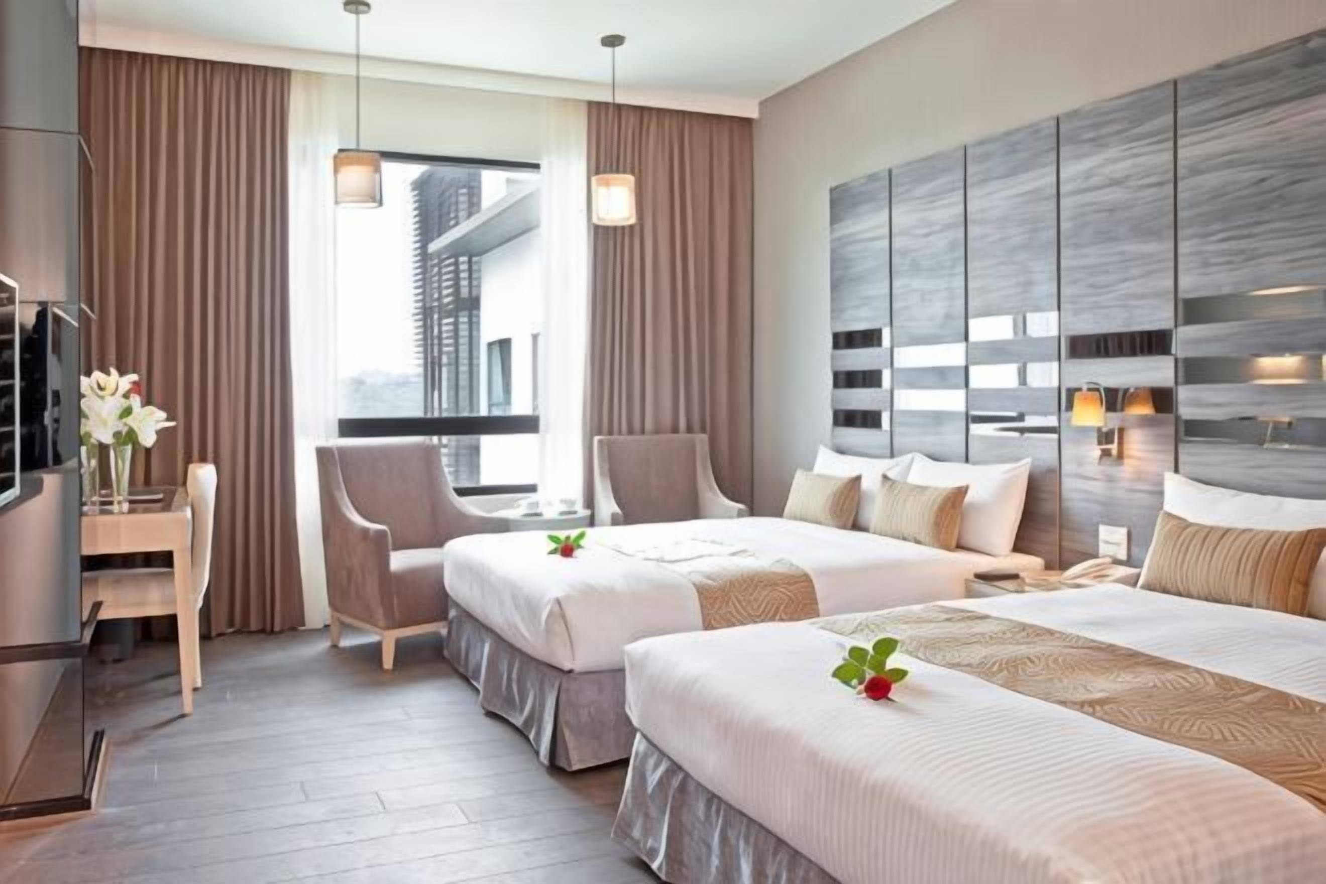 A hotel room with two beds, a desk, a chair, a TV, and a view of a building.