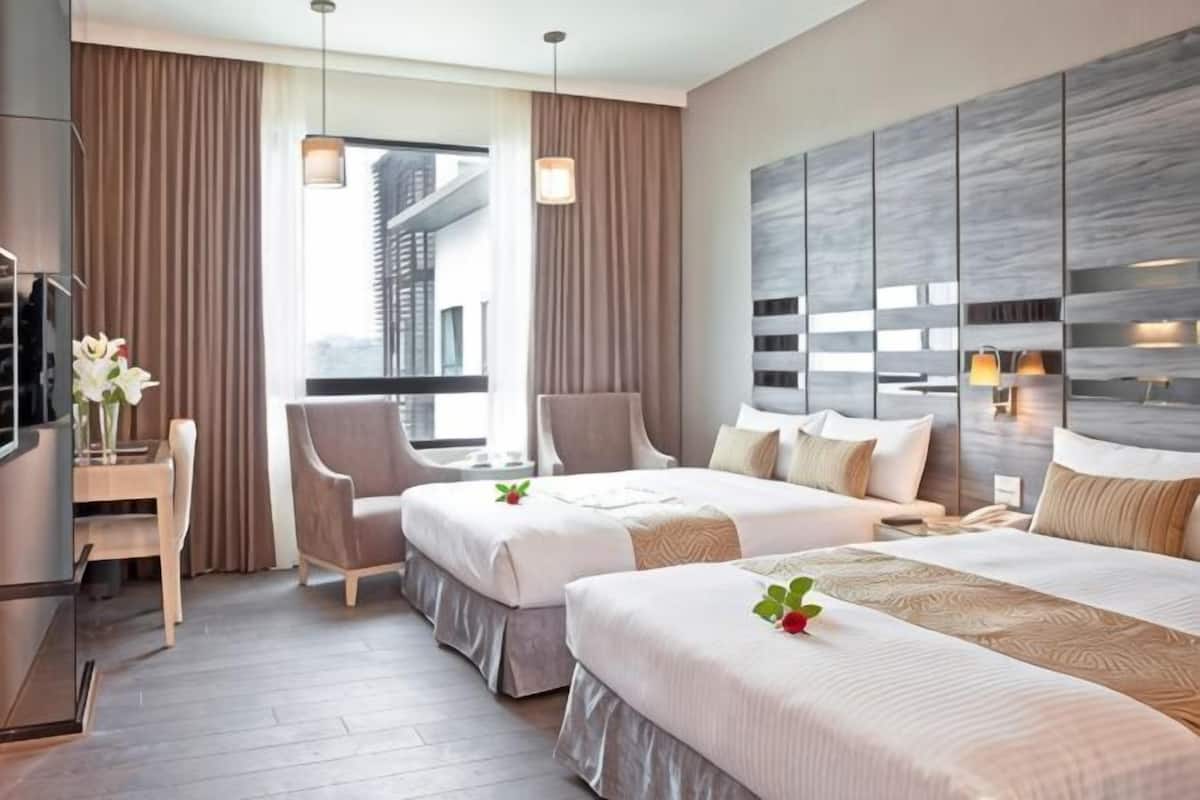 A hotel room with two beds, a desk, a chair, a TV, and a view of a building.