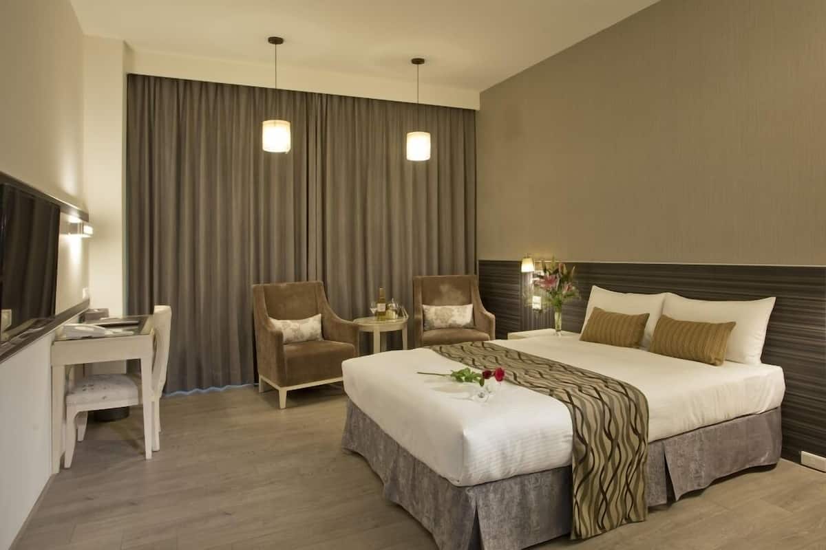 A hotel room with a large bed, two armchairs, a small table, and a desk.