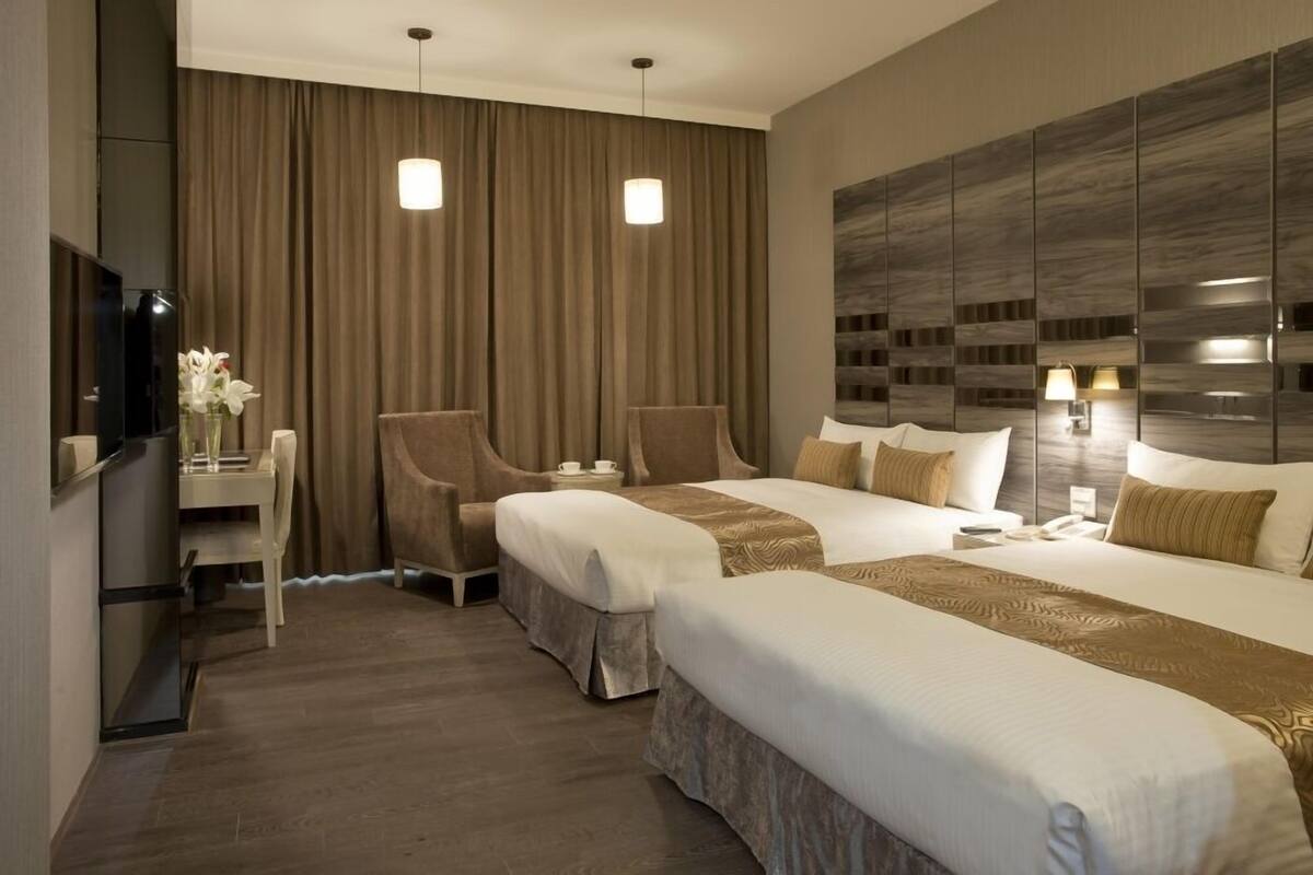 A hotel room with two beds, a desk, a chair, a TV, and a large wall unit.