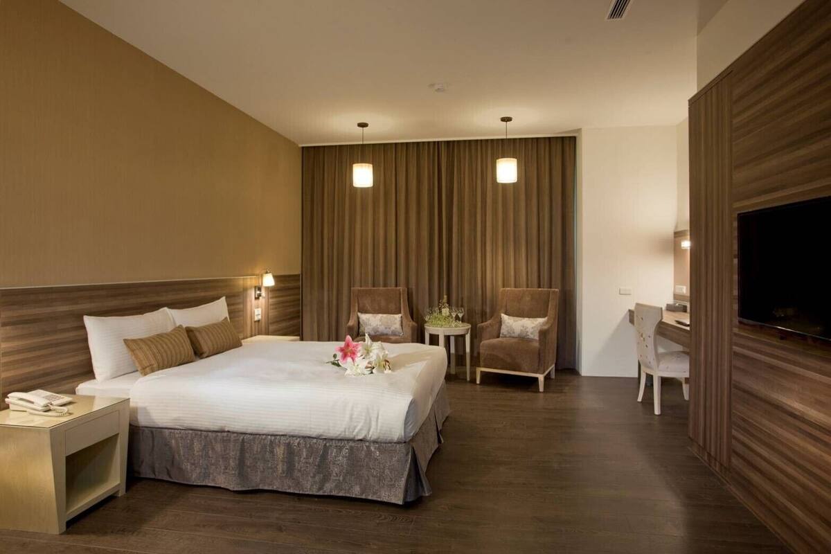 A hotel room with a large bed, two chairs, a desk, and a TV.