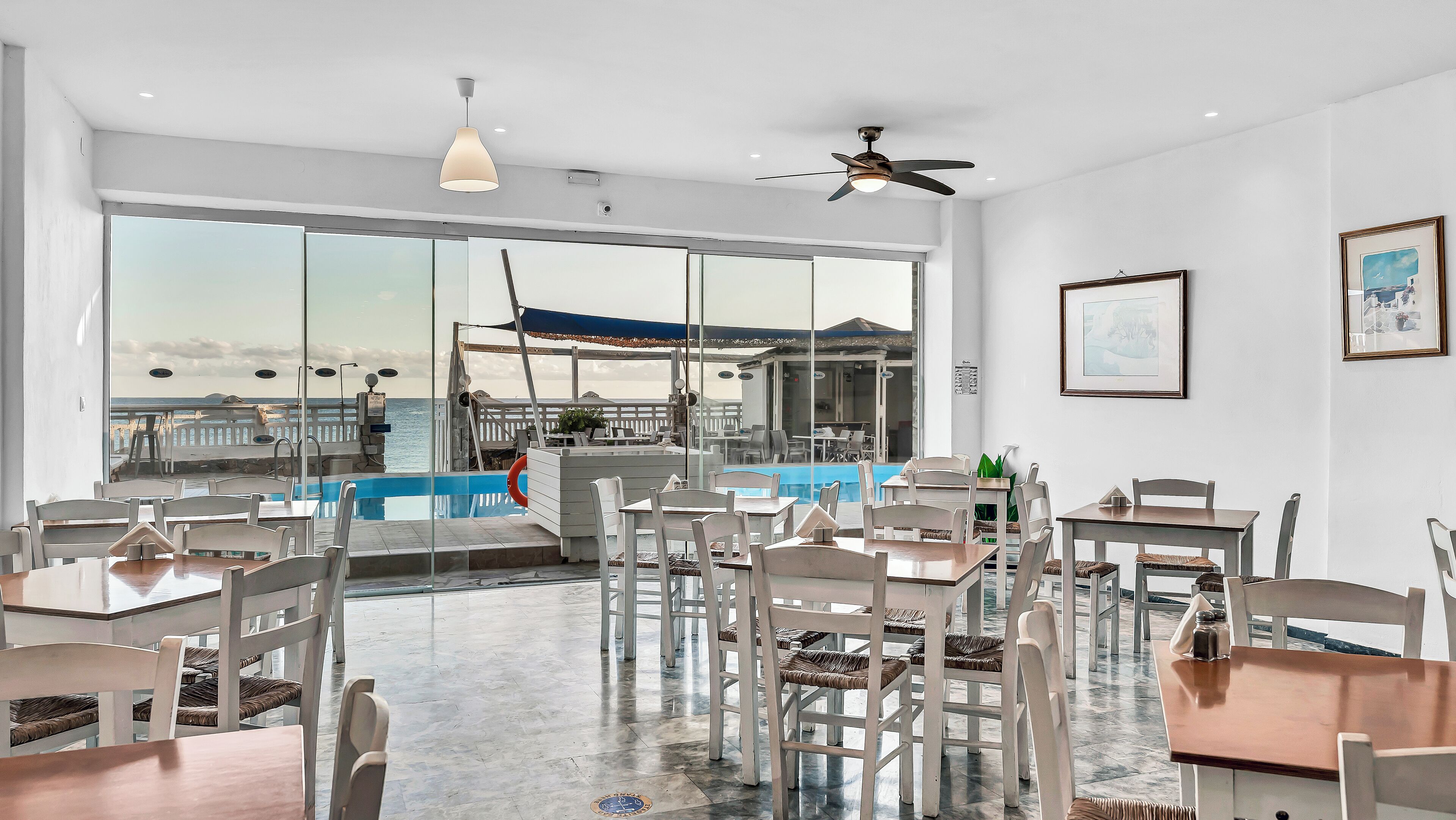 A spacious indoor area with a pool, dining tables, and chairs, featuring large windows and a ceiling fan.