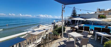 A seaside patio with outdoor seating, a pool, and a view of the ocean.