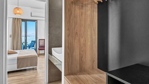 Habitación de hotel moderna con cama, una silla, una mesita y vista al mar a través de un ventanal grande.