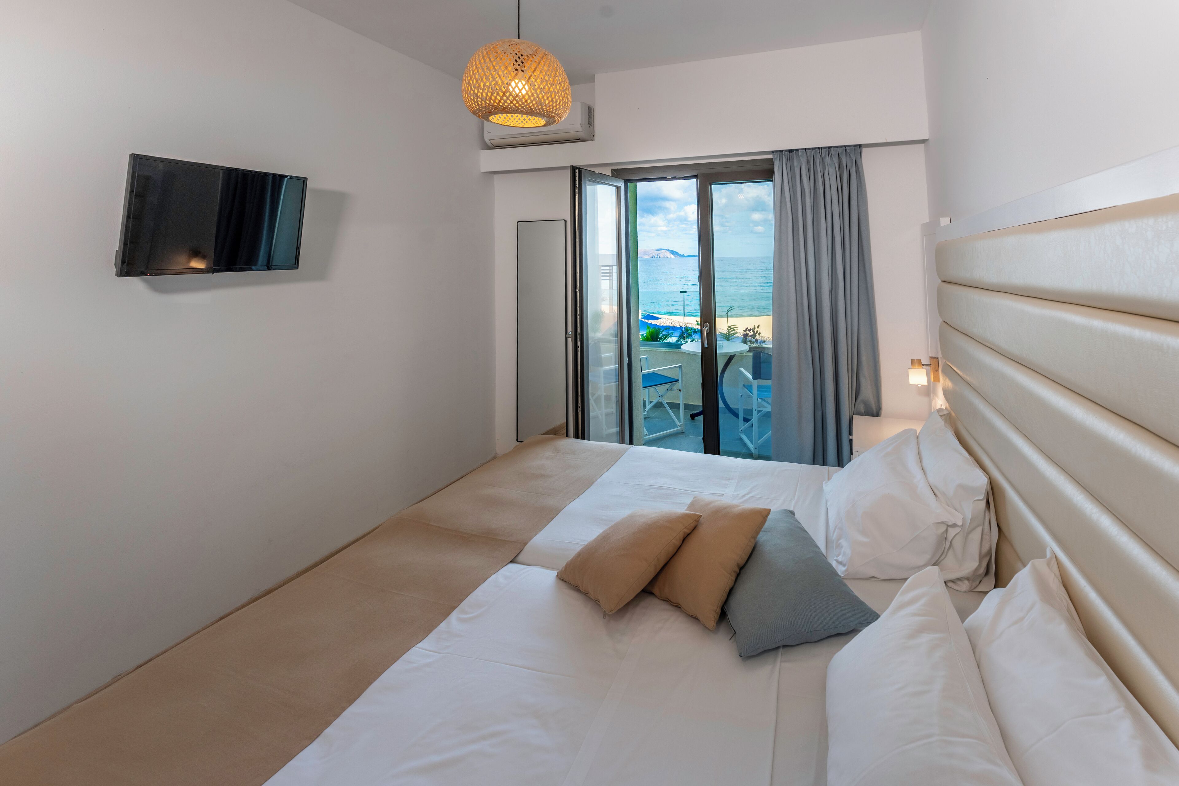 Ein modernes Hotelzimmer mit einem großen Bett, einem flachbildfernseher an der Wand und Blick auf den Strand durch Glastüren.