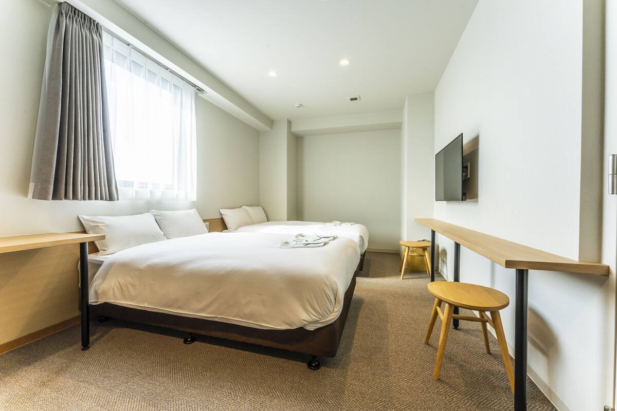 A hotel room with a bed, a desk, a chair, a TV, and a window with curtains.