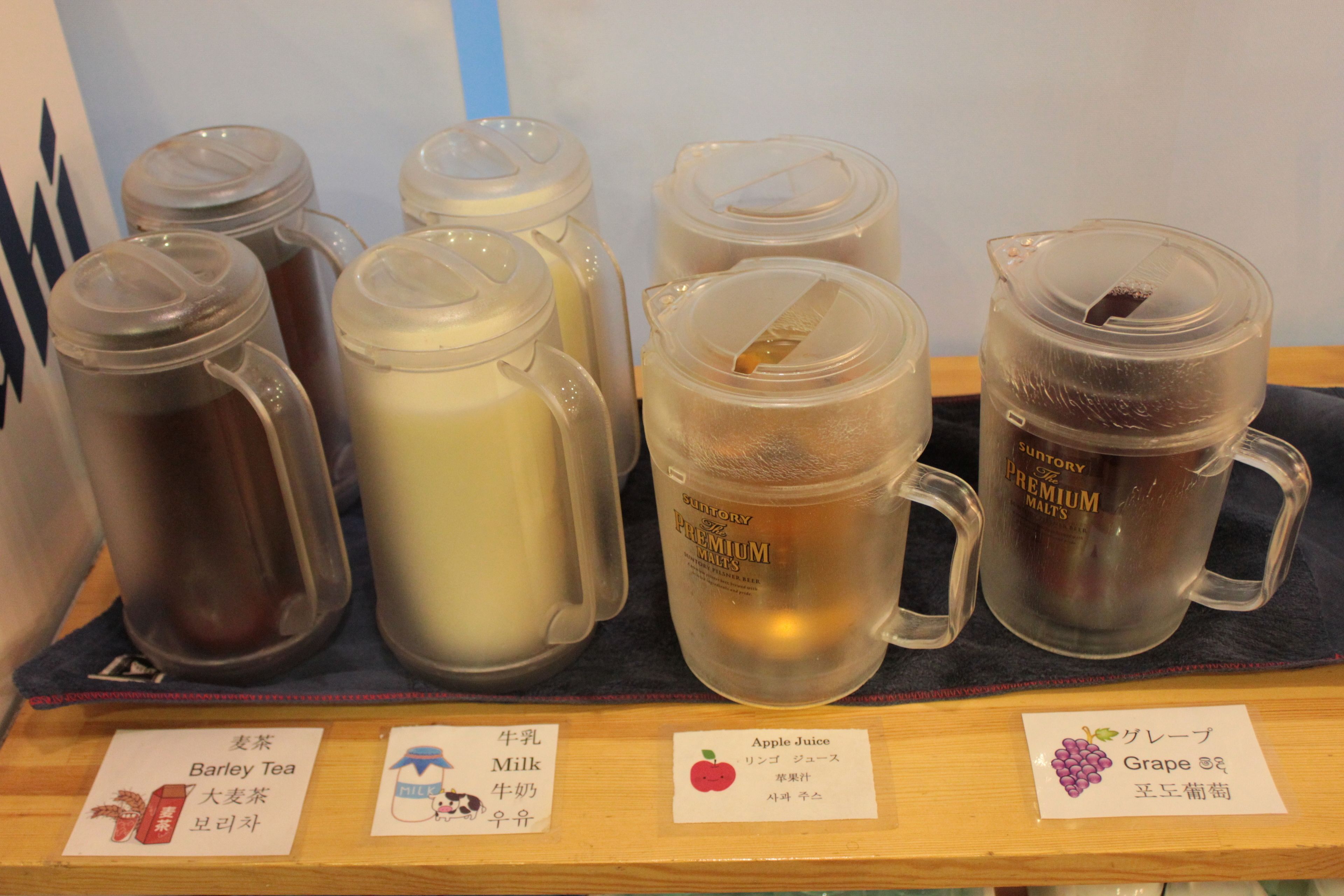 A selection of beverages including barley tea, milk, apple juice, and grape juice, each labeled in both English and Japanese.