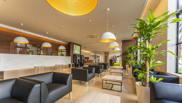 A modern hotel lobby with black leather sofas, wooden flooring, and large potted plants. - CVS Bay Hotel (Ichikawa)