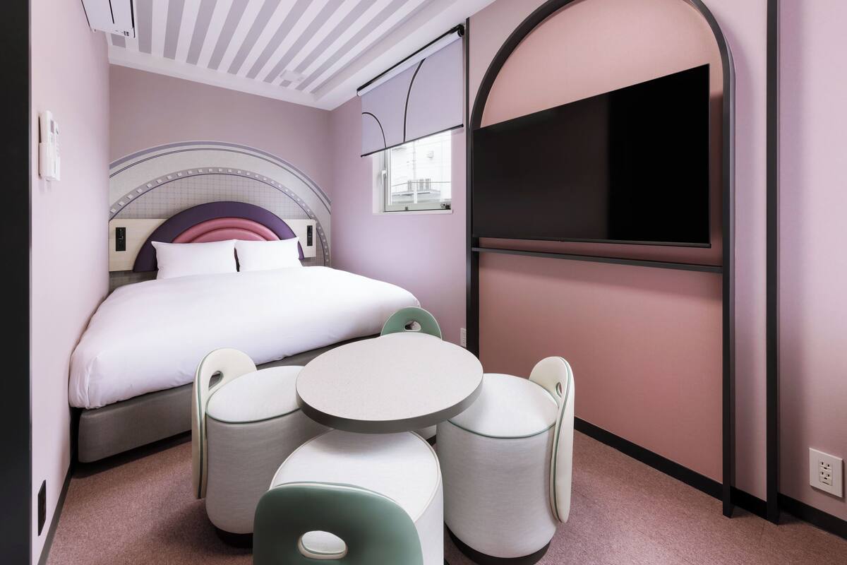 A modern hotel room with a bed, a TV, a small table, and seating.