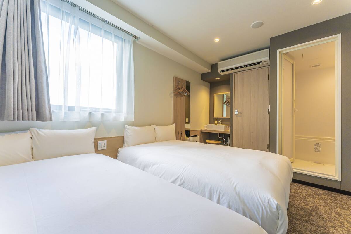 A hotel room with two large beds, a bathroom with a shower, and a walk-in closet.