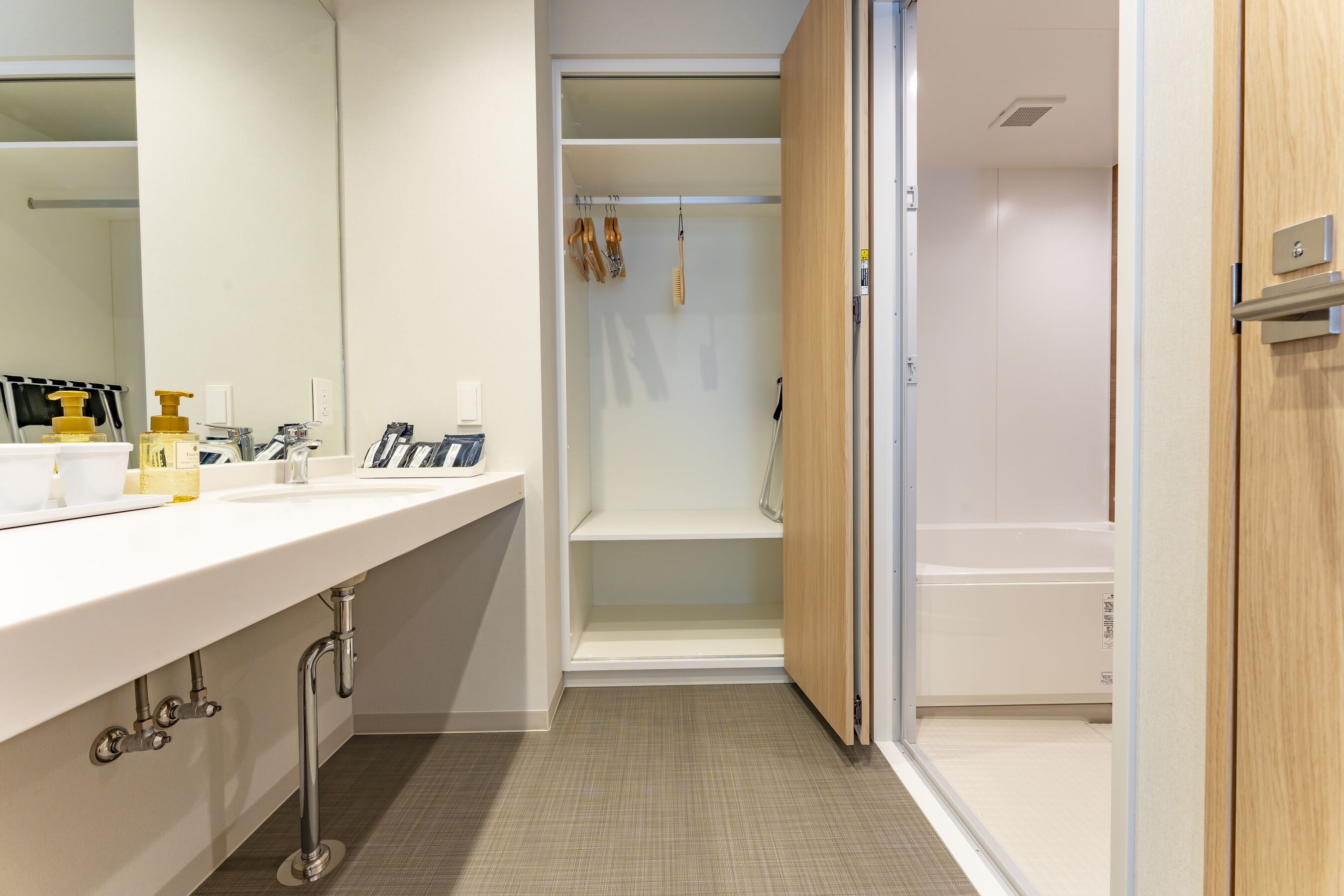 Un baño moderno con un tocador blanco, una zona de ducha y una puerta de madera.