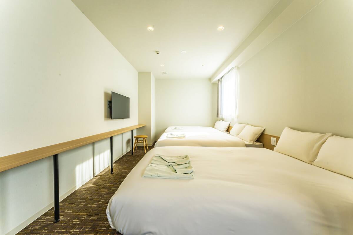 A hotel room with two beds, a flat-screen TV mounted on the wall, and a wooden bench.