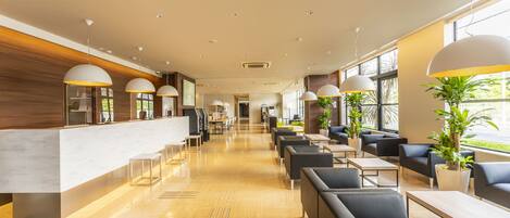 A modern hotel lobby with a reception desk, seating area, and large windows.