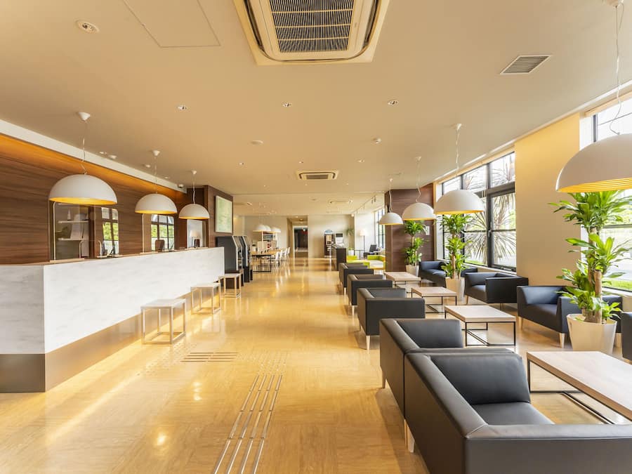 A modern hotel lobby with a reception desk, seating area, and large windows.