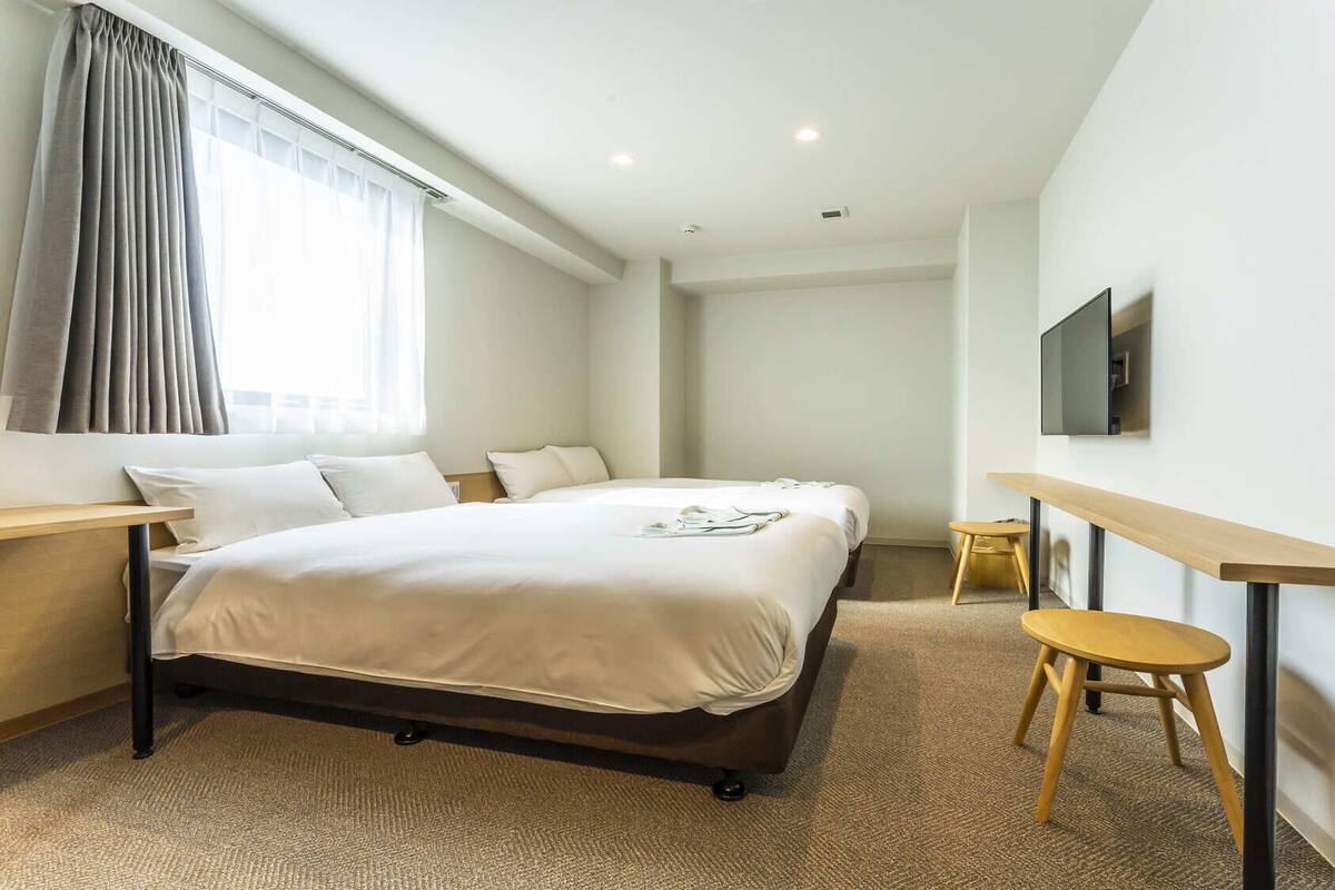 A hotel room with a bed, a desk, a chair, a TV, and a window with curtains.