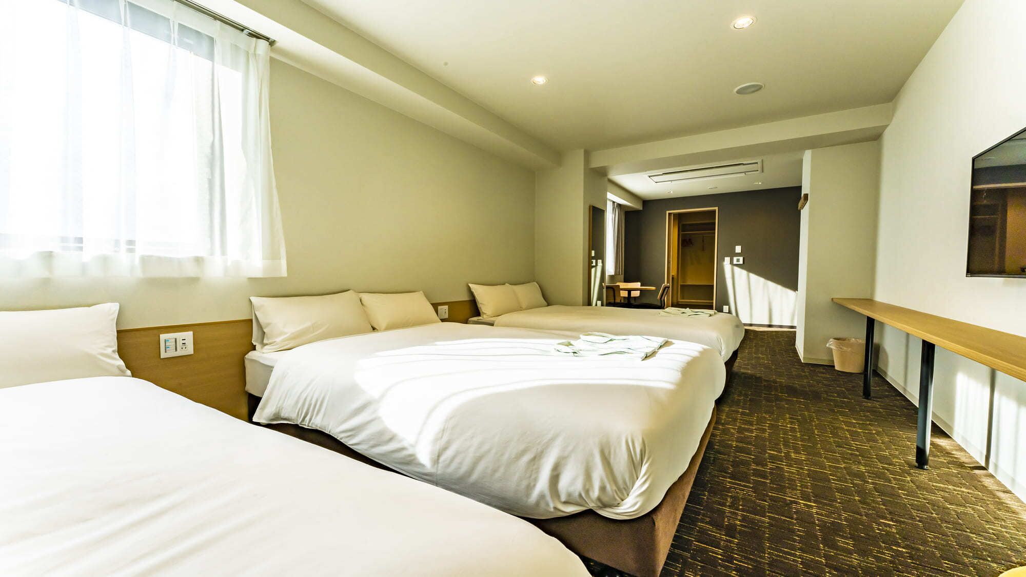 A hotel room with two beds, a wooden headboard, a small table, and a mirror on the wall.