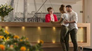 A reception area with a wooden reception desk, a large window with a view of a bridge, and a potted plant with yellow flowers.