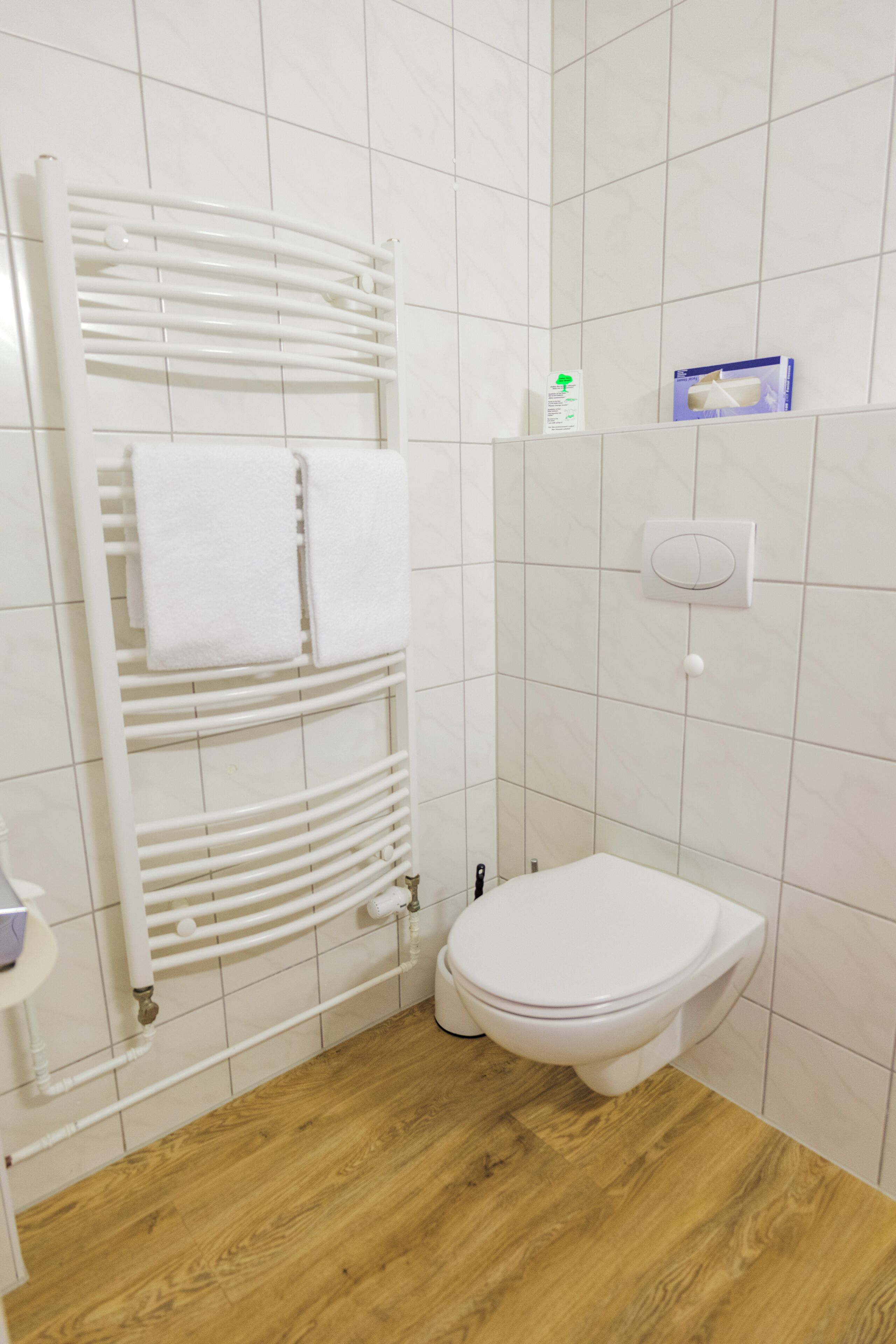 A bathroom with a white toilet, a towel rack with two towels, a white radiator, and a blue box on the wall.