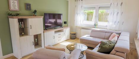 Ein Wohnzimmer mit einer Couch, Sesseln, einem Fernseher und einem Schrank.