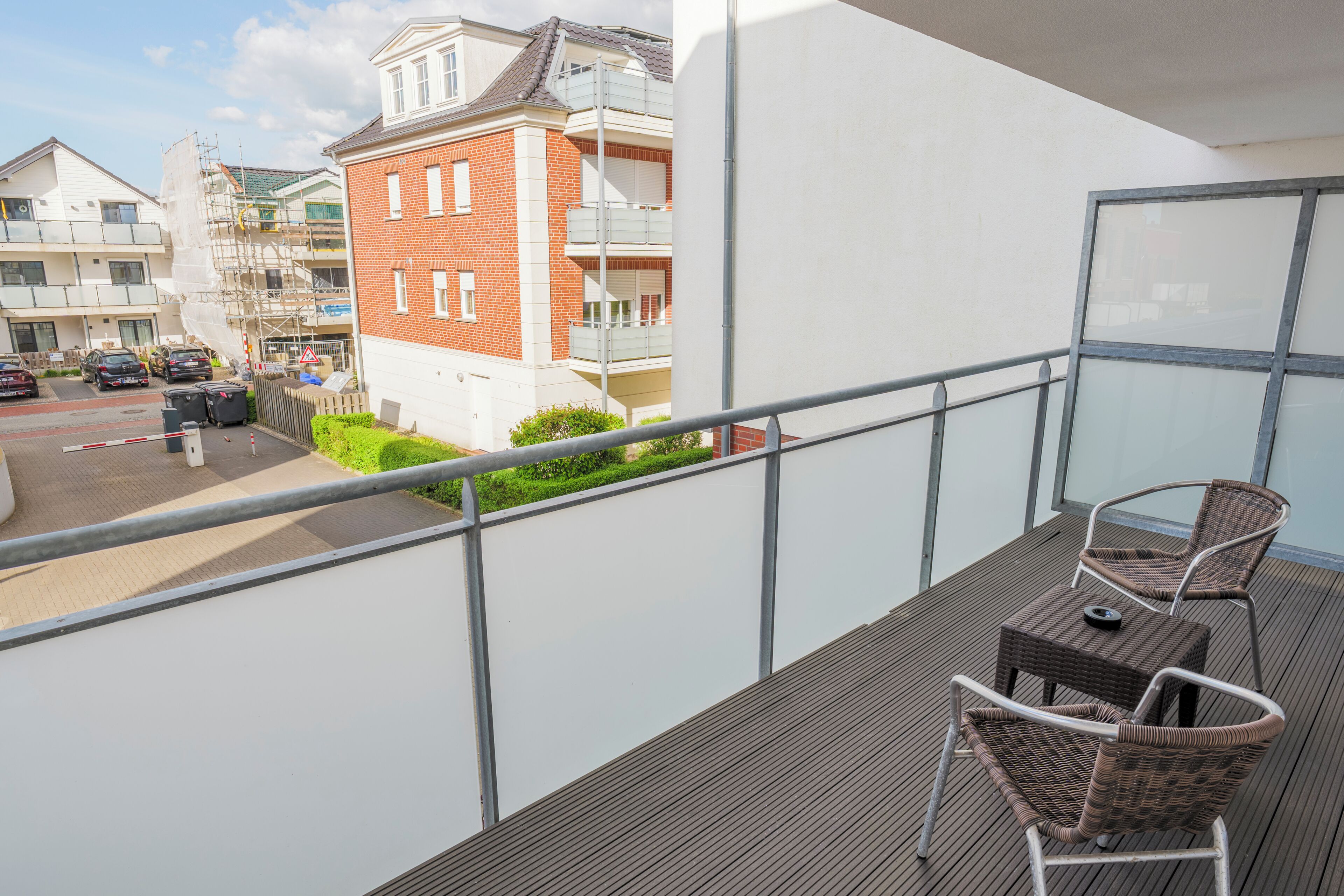 Ein Balkon mit Blick auf eine Straße, ein rot Backsteinhaus und einen klaren Himmel.