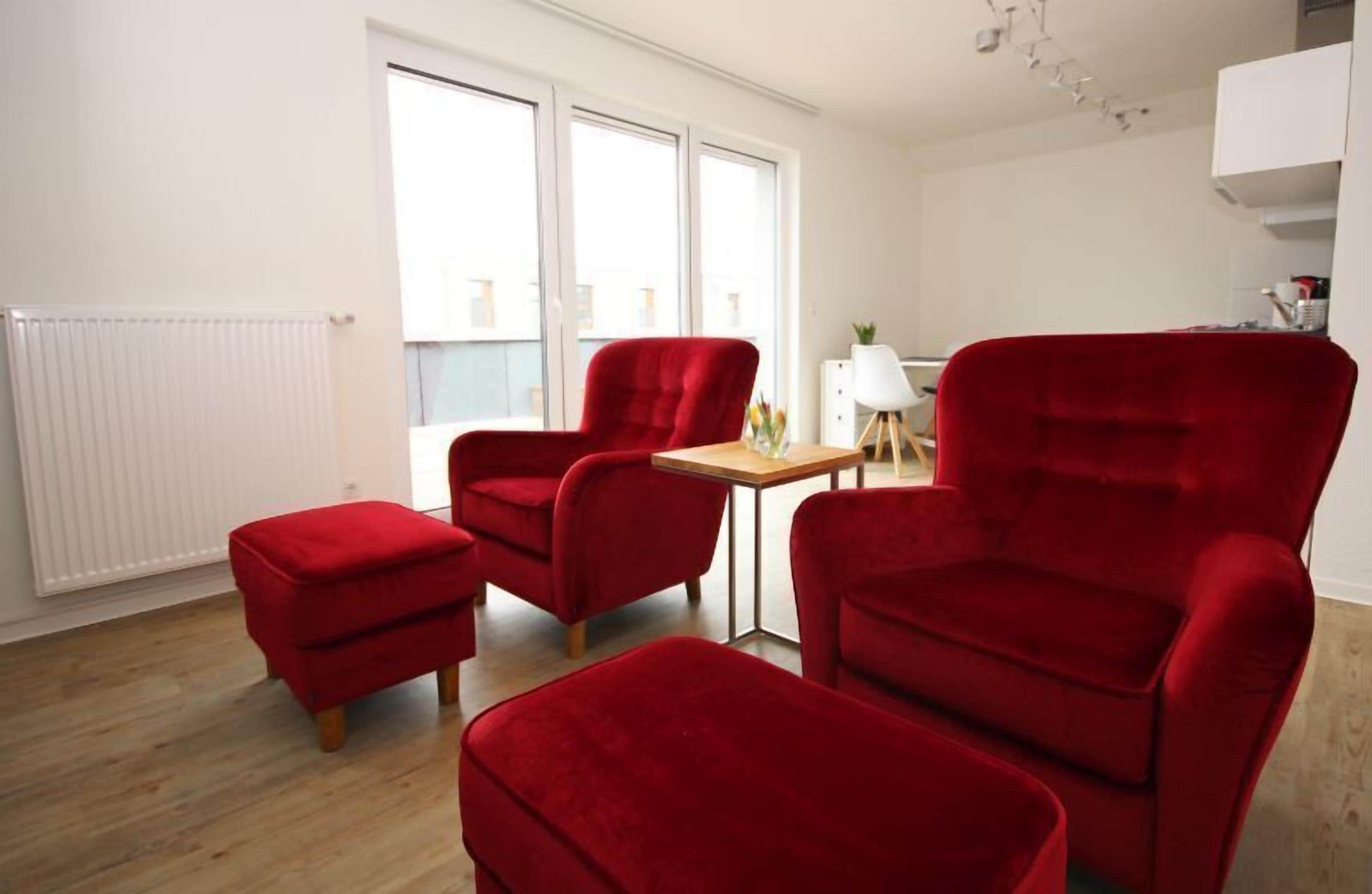 A modern living room with red velvet armchairs, a wooden coffee table, and a white radiator.