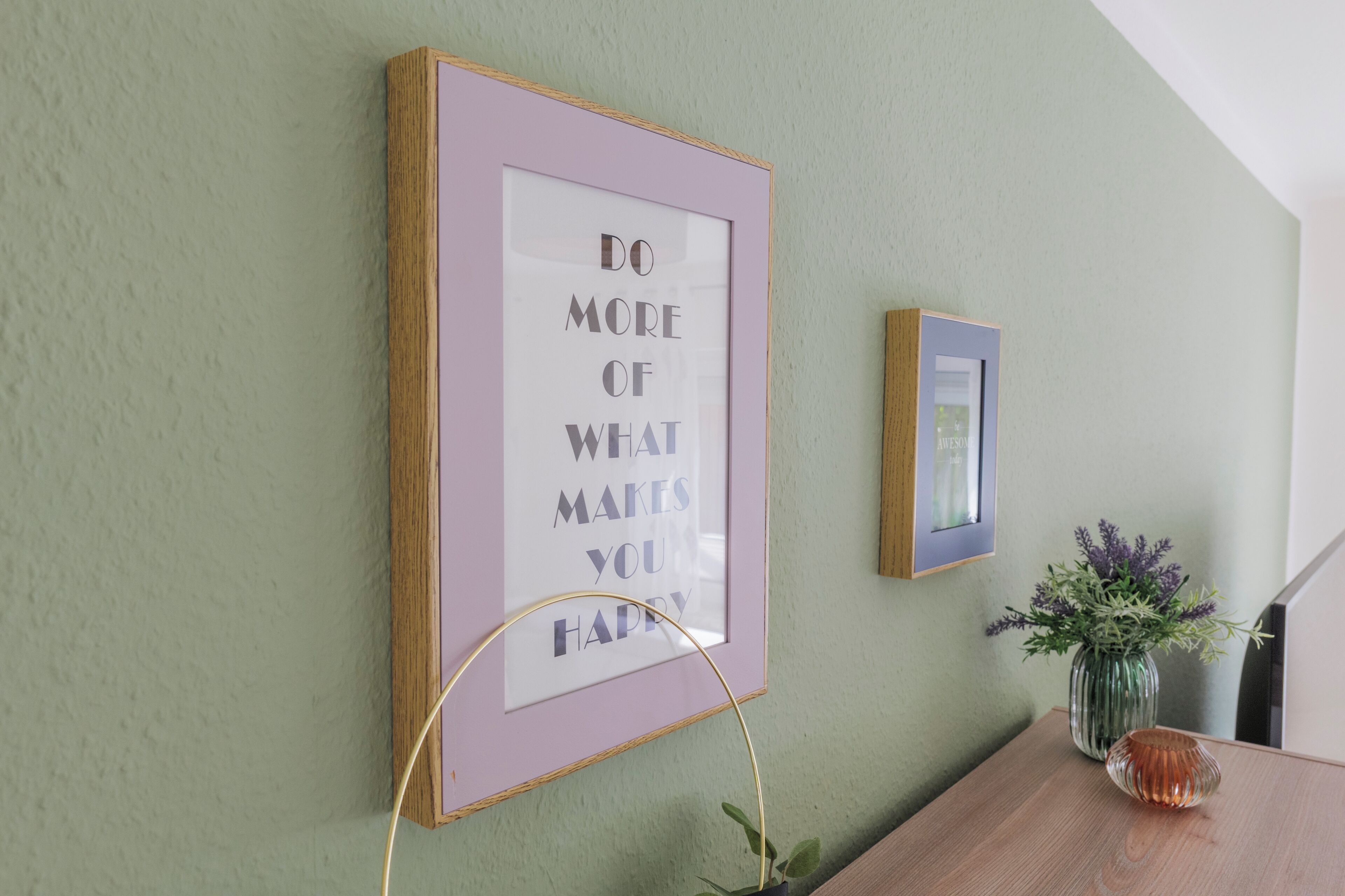 A framed motivational quote on a wall, a small framed picture, and a vase with flowers on a wooden table.