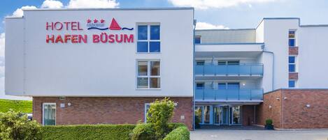 Un moderno edificio de hotel con un cartel que dice "HOTEL HAFEN BÜSUM" y un logotipo con tres estrellas y una montaña.