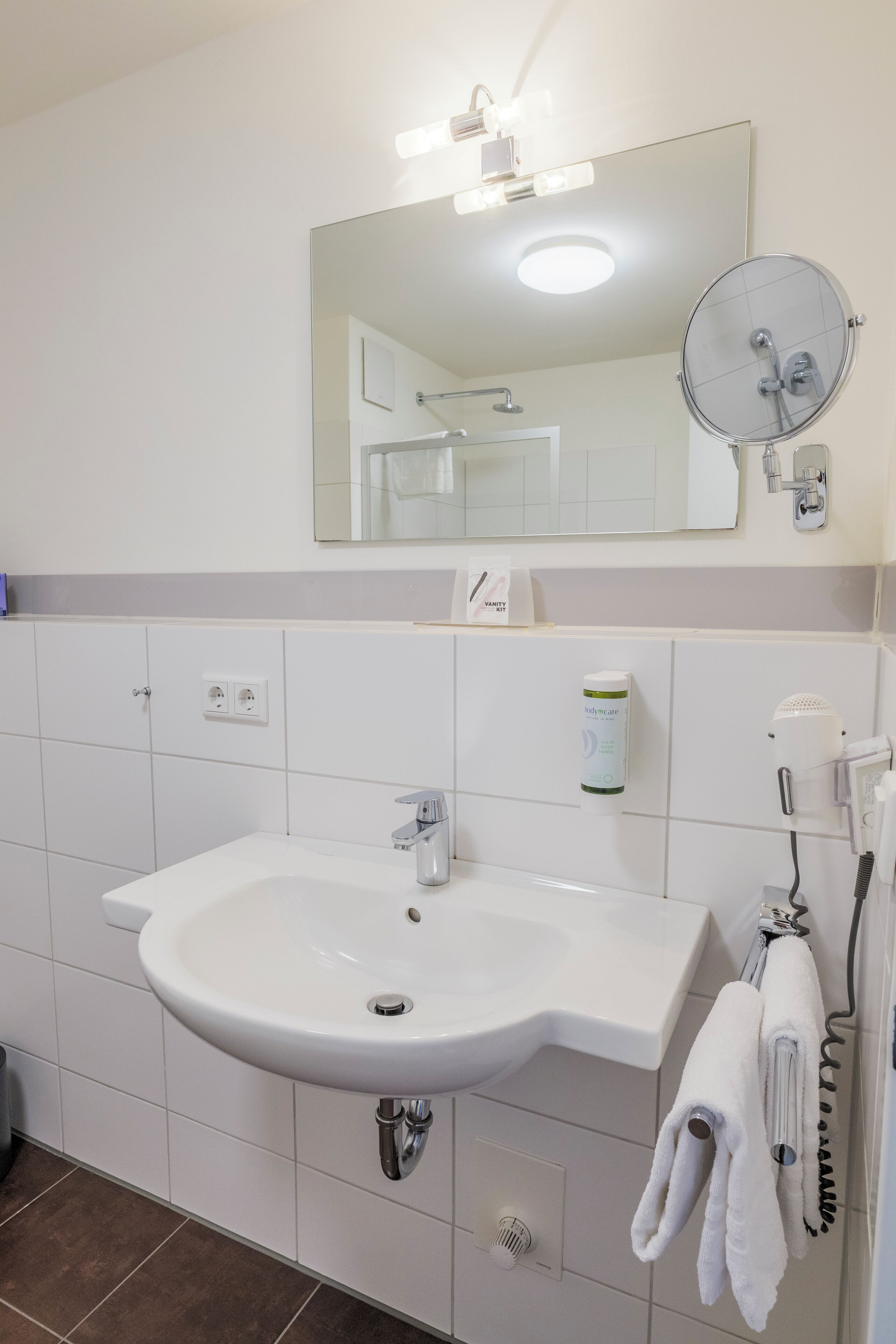 Un baño con lavamanos blanco, un espejo, toallero y secador de pelo.