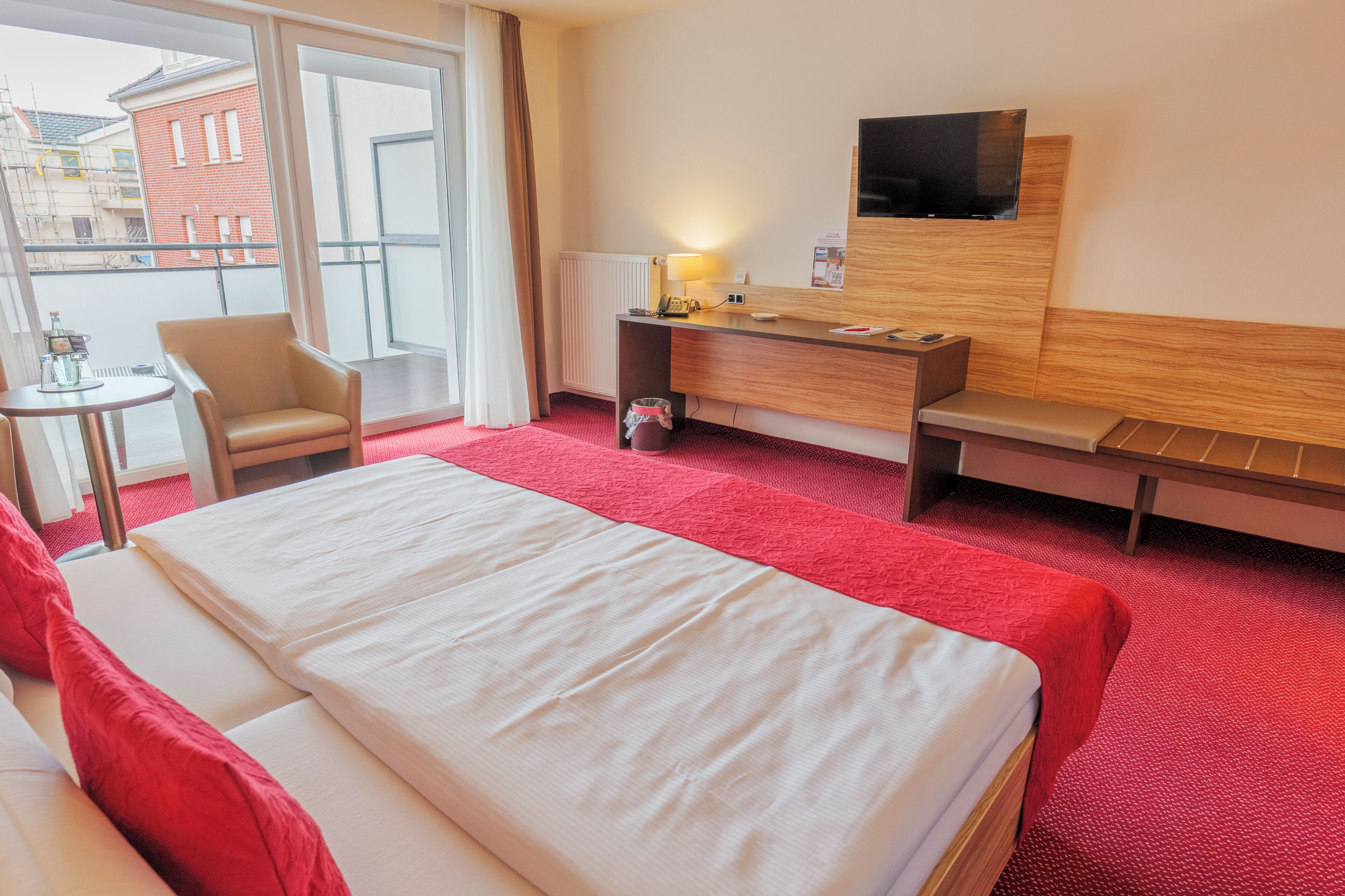 A hotel room with a bed, a desk, a chair, a TV, and a view of the outside.