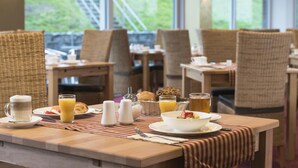 Desayuno con sillas de mimbre, una mesa de madera y vistas a la vegetación.