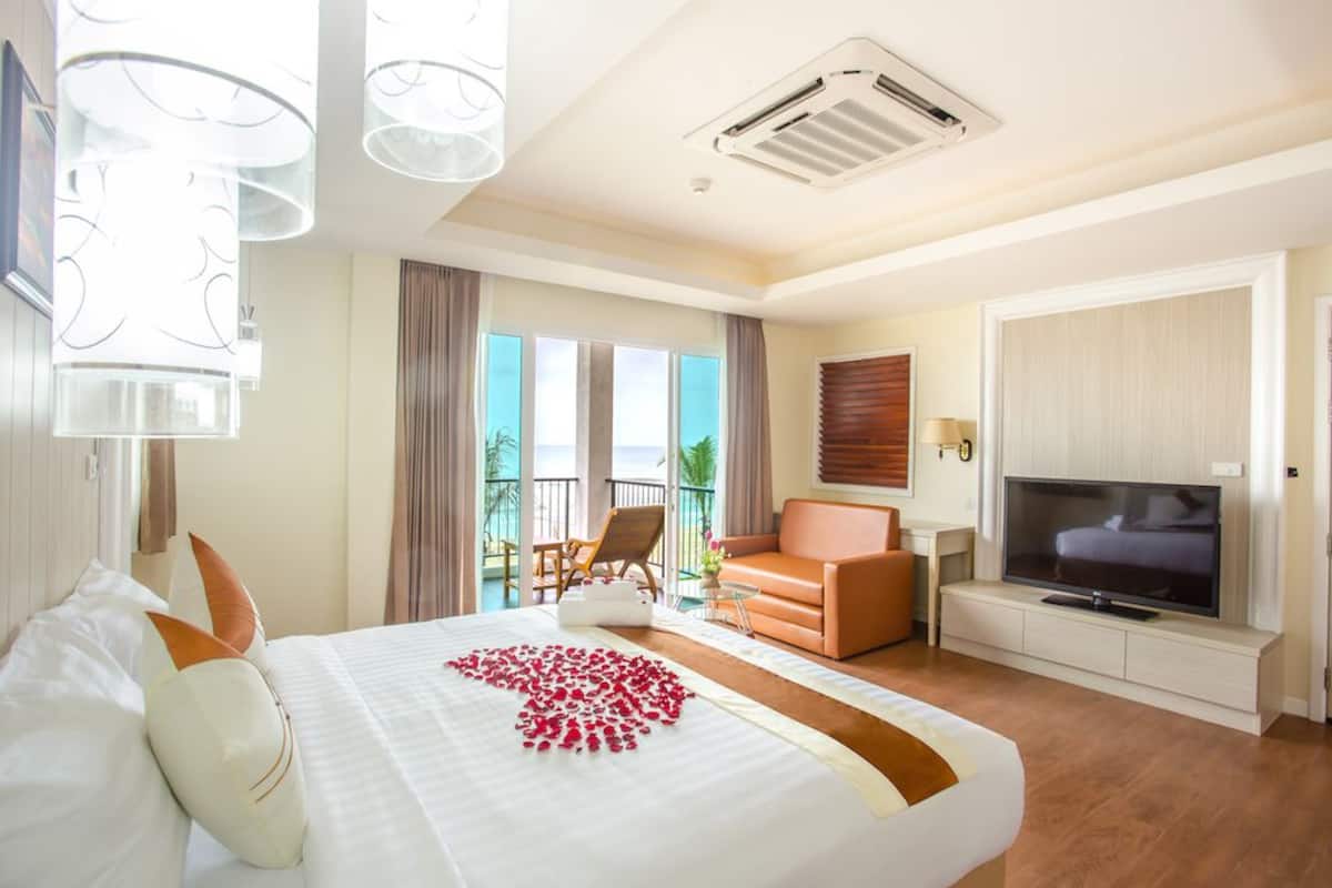 Habitación de hotel con cama, televisor, balcón con una silla y vista al mar.