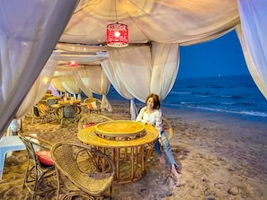 Montaje para comer frente a la playa, con mobiliario de mimbre y un farol rojo.