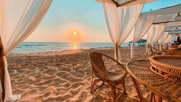 A beachside setting with a wicker table and chairs under a canopy, overlooking the ocean at sunset. - Saint Tropez Beach Resort Hotel (Tha Mai)