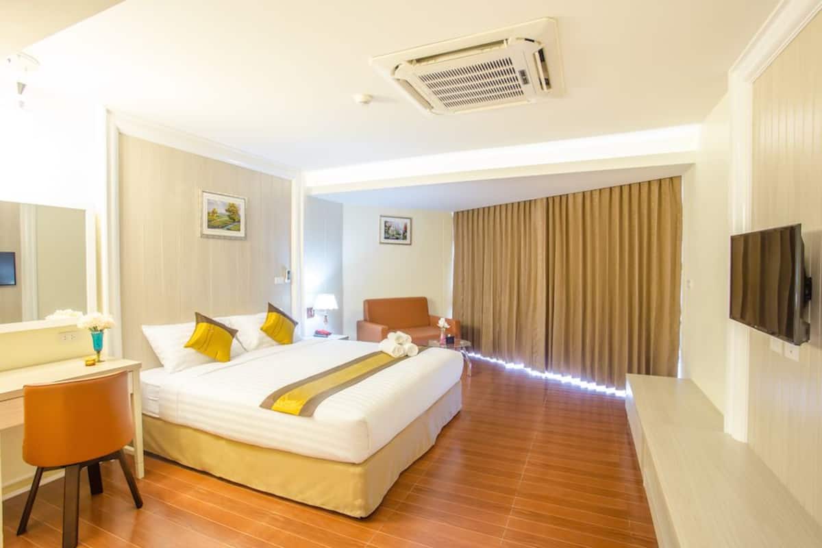 Habitación de hotel con una cama grande, un escritorio, una silla, un televisor y un baño visible a través de una puerta abierta.