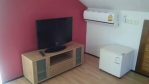 A small room with a wooden TV stand, a flat-screen TV, a white mini-fridge, and a red wall. - Ma Maison Phuket (Choeng Thale)