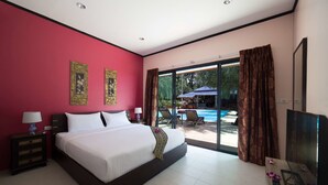 A hotel room with a large bed, a TV, and a view of a swimming pool and outdoor seating. - Ma Maison Phuket (Choeng Thale)