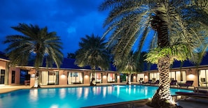 A swimming pool surrounded by palm trees and a building with multiple rooms.