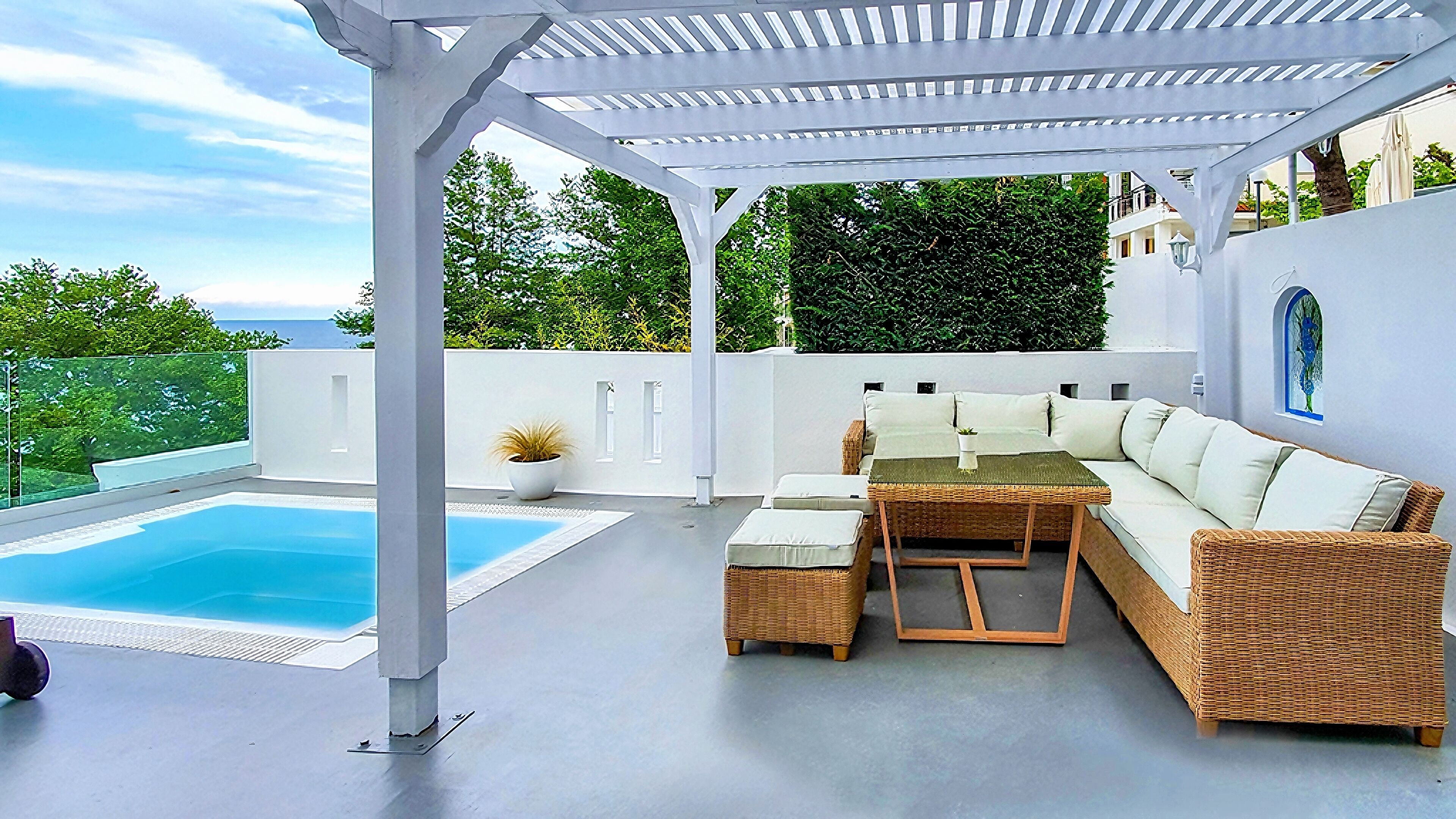 A covered outdoor area with a pool, a wicker sofa, and a table.