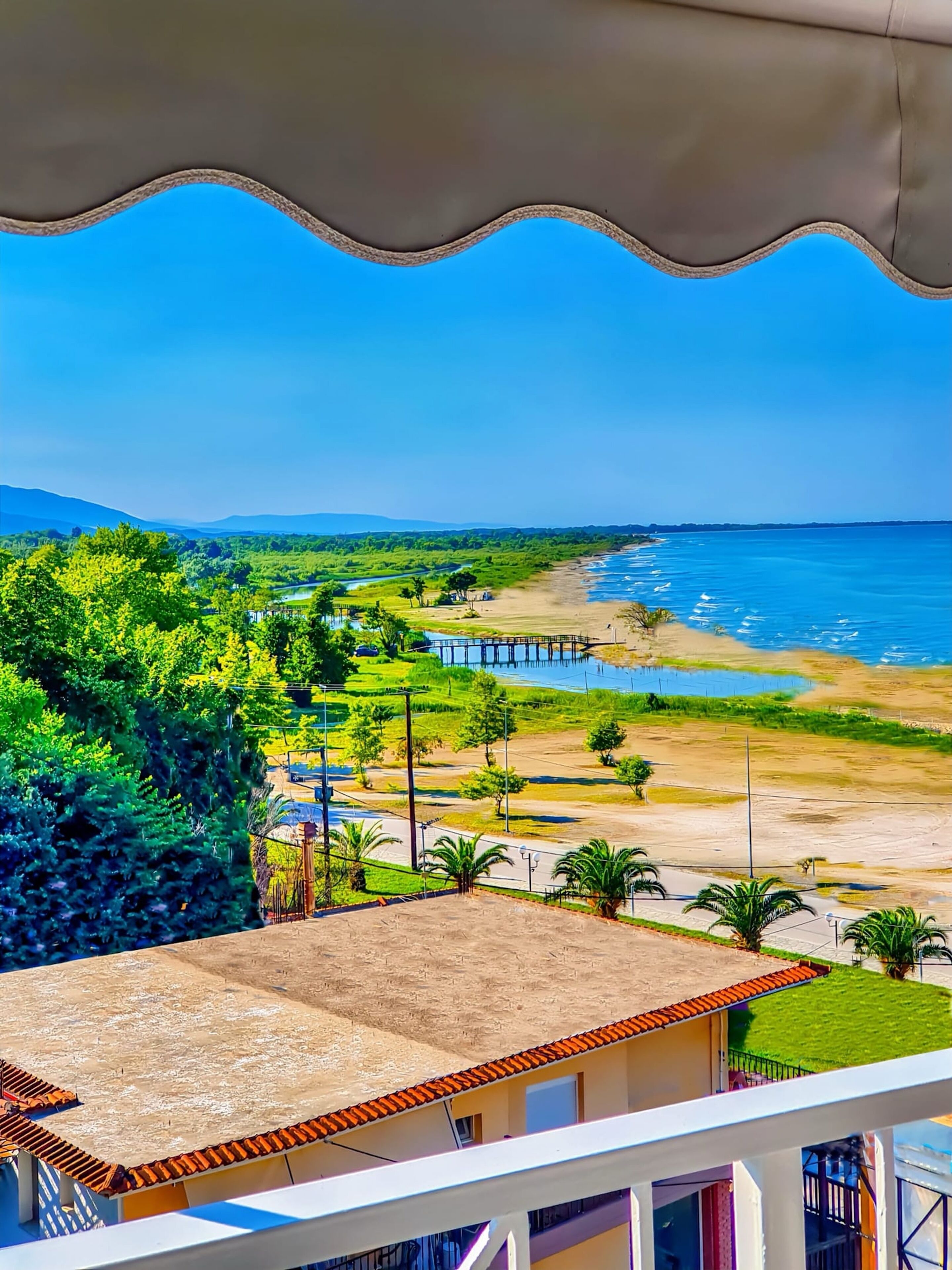 Une vue sur la côte depuis un balcon, avec une plage, des palmiers et une jetée.