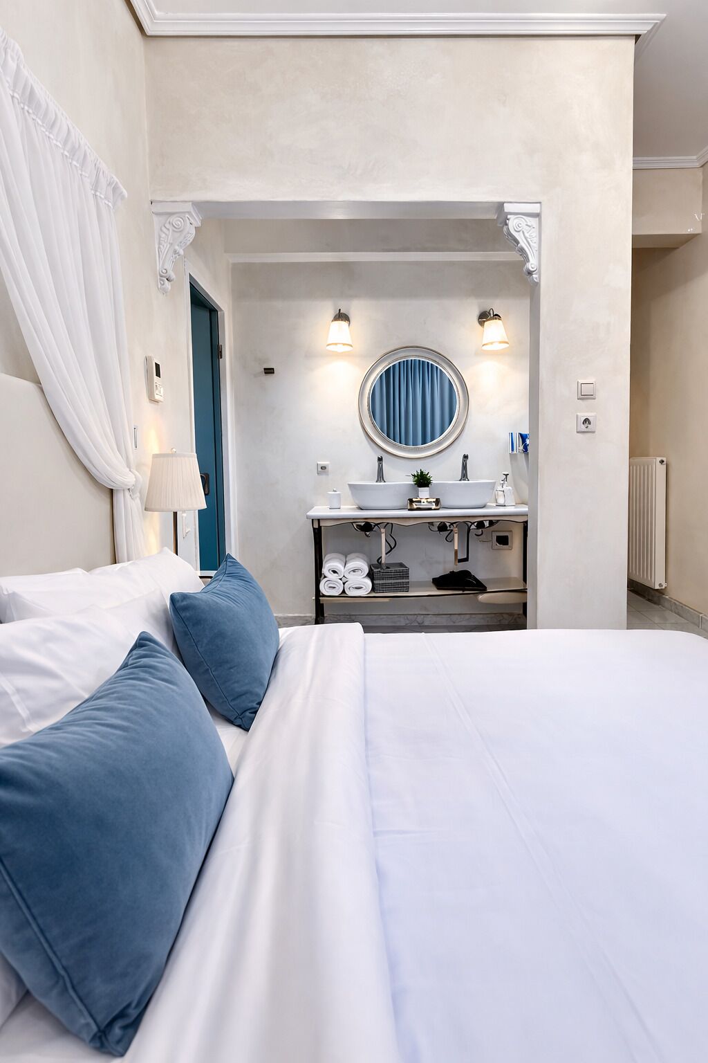Une chambre d’hôtel avec un lit, une salle de bain dotée d’un miroir rond et un rideau bleu.