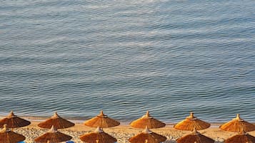Uma praia com fileiras de guarda-sóis de palha e cadeiras de praia azuis.