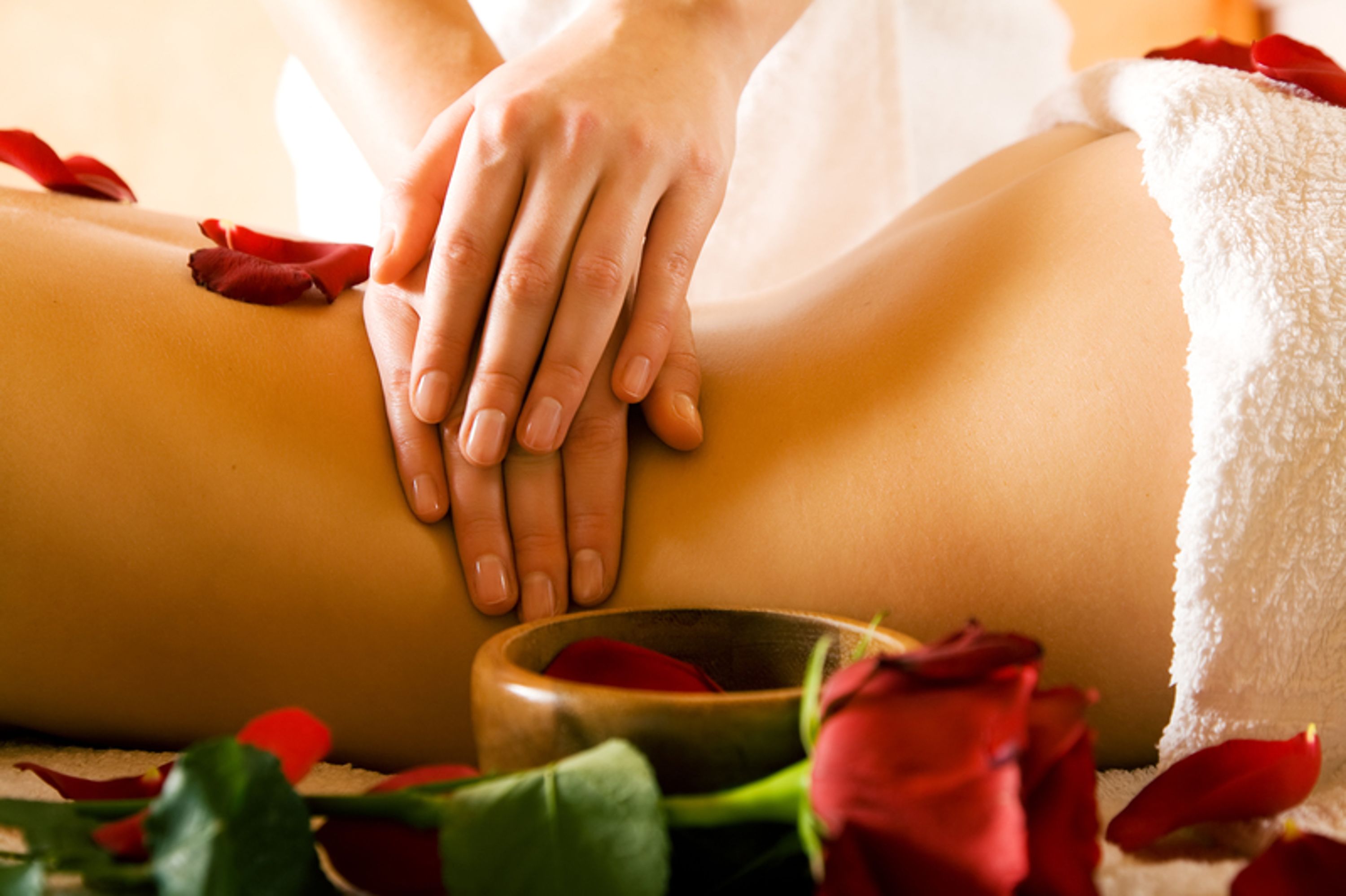 Eine Nahaufnahme einer Massage mit Rosenblättern und einer Holzkugel.