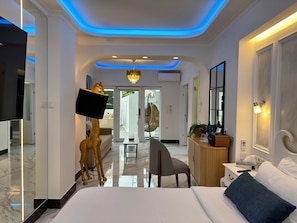 A modern hotel room with a bed, a desk, a chair, a television, and a decorative golden giraffe statue. - Panorama Suites & Spa (Agia)