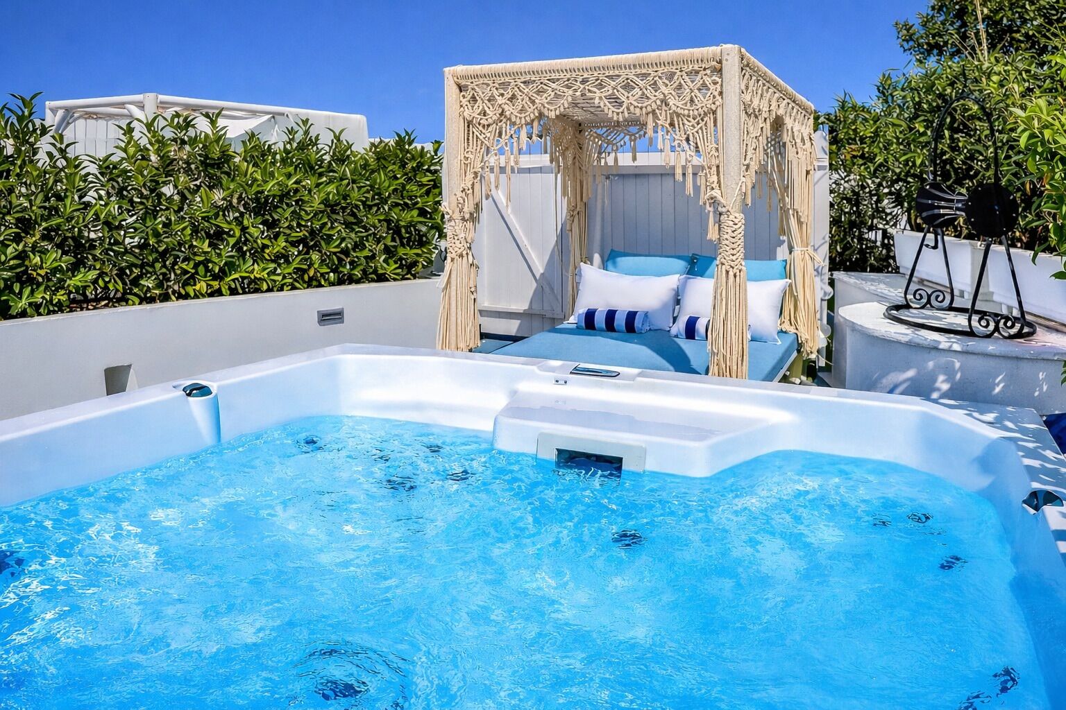 Een bubbelbad met een zonnescherm, een lounge stoel en een zwembadgedeelte met uitzicht op de lucht en begroeiing.
