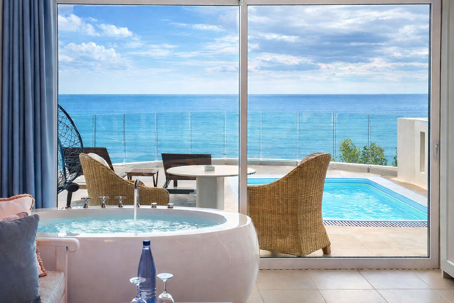 Un balcón con jacuzzi, sillas de mimbre, una mesa y vista al océano.