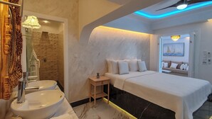 A modern bedroom with a large bed, a vanity with a sink, and a shower area. - Panorama Suites & Spa (Agia)