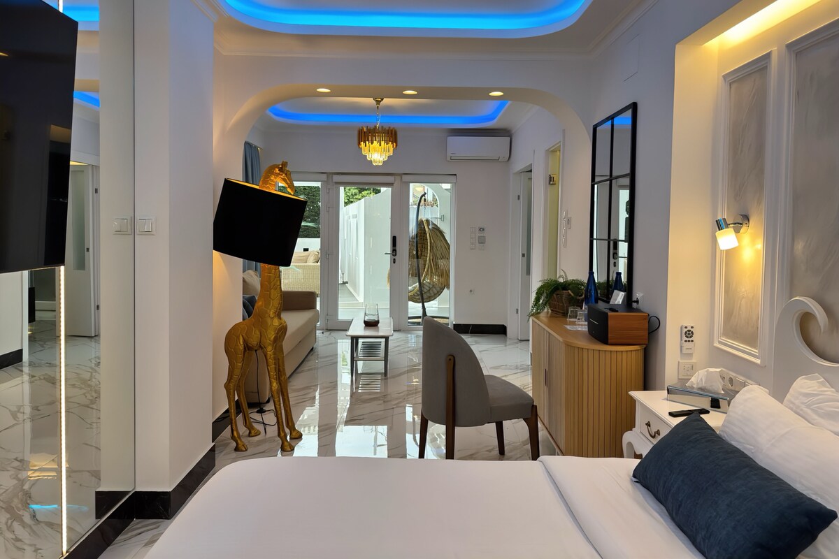 A modern hotel room with a bed, a desk, a chair, a TV mounted on the wall, and a decorative golden giraffe statue.