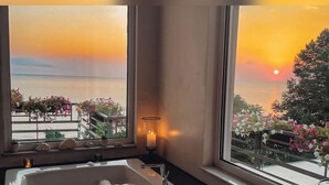 A bathtub with a view of the sunset and a balcony with flowers. - Panorama Suites & Spa (Agia)