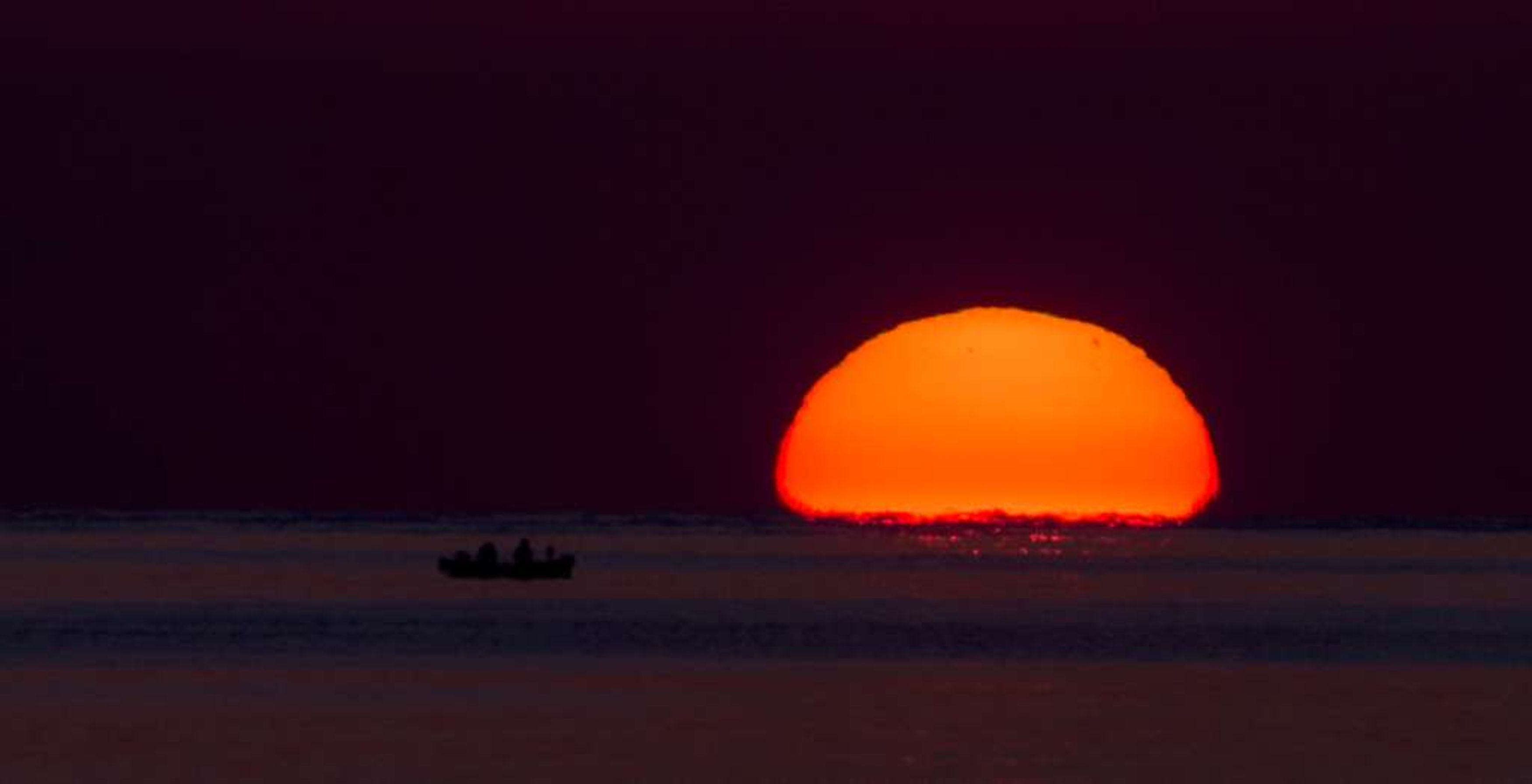Um pôr do sol sobre águas calmas com um pequeno barco ao primeiro plano.